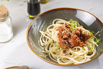 Italian spaghetti with bolognese tomato sauce and fresh thyme in dark green bowl on white concrete surface, with olive oil and balsamic vinegar in the back