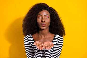 Photo portrait of curly girl in striped shirt sending air kiss with pouted lips isolated vibrant yellow color background