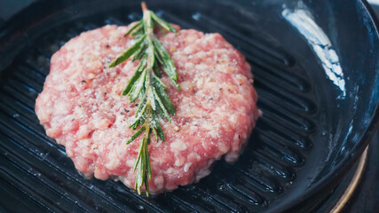 close up of mince patty with salt and rosemary branch on hot pan