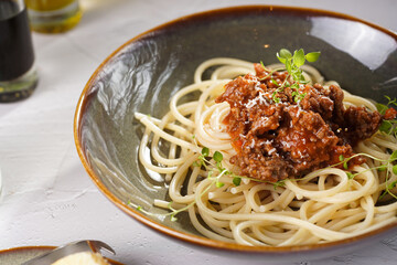 Italian spaghetti with bolognese tomato sauce and fresh thyme in dark green bowl on white concrete surface, with olive oil and balsamic vinegar in the back