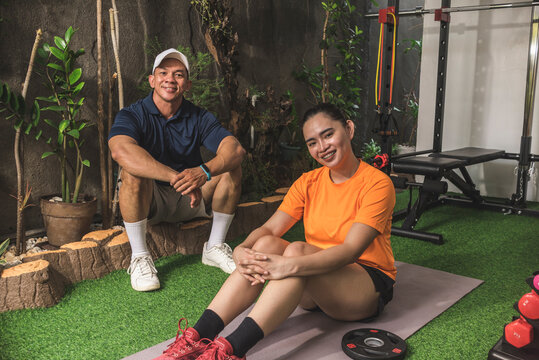 A happy personal trainer and his pretty client at an indoor garden converted intro a home gym. - Powered by Adobe