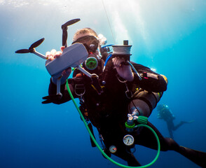 Women diver with drone underwater shooting on a blue background. Diver with tech equipement