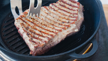 close up of cooking tongs near beef steak on grill pan