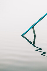 Blue handrail of stairs leading into a foggy lake and its curved reflection on the surface of the...