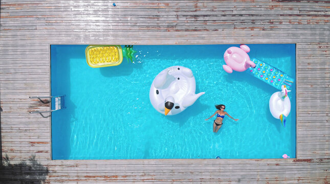 AERIAL. woman having fun on the air mattress in the swimming pool. Different inflatable beds of various colors and shapes