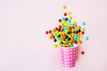 Paper cup with tasty candies on color background