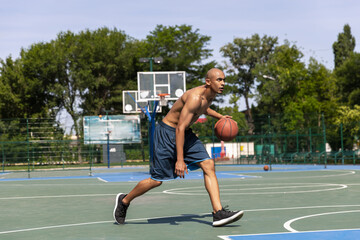 Obraz premium Strong muscular african-american male basketball player training at street public stadium, sport court or palyground outdoors. Summer sport games.
