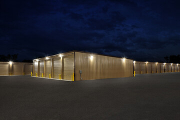 Large lit industrial storage warehouse complex with brown warehouse buildings at night