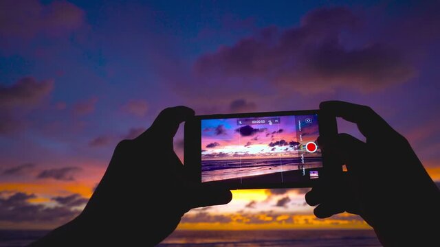 Travel video. Close-up screen smart phone take a photo and video sunset on beach Travel on vacation at a beach and sunset time.  The most beautiful sunset of the sea in summer sun in Phuket, Thailand.