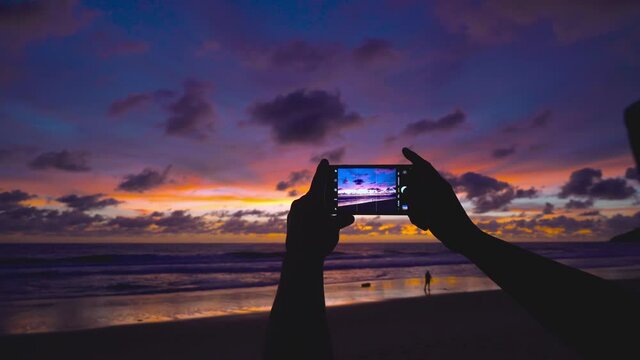 Travel video. Close-up screen smart phone take a photo and video sunset on beach Travel on vacation at a beach and sunset time.  The most beautiful sunset of the sea in summer sun in Phuket, Thailand.