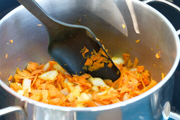 Carrots and onions are stewed in a saucepan. Stir with a spoon.