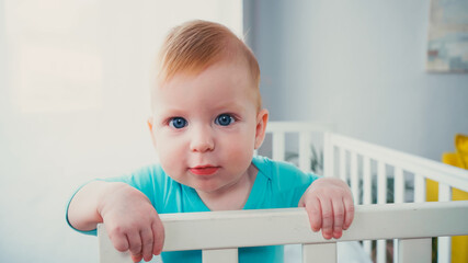infant boy standing in baby crib and looking at camera