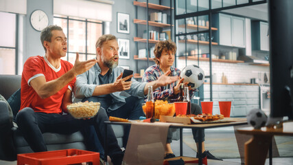 Obraz premium At Home Three Soccer Fans on Couch Watch Sport Game on TV, Use Smartphone App to Online Bet, Annoyed After Referee Decision. Friends Cheer Eat Snacks, Watch Favourite Football Club Play.