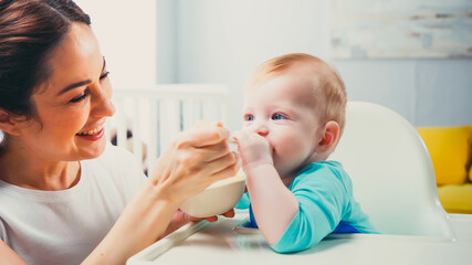 Obraz na płótnie Canvas cheerful mother smiling while feeding infant son