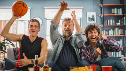At Home Three Joyful Basketball Fans Sitting on a Couch Watch Basketball Game on TV, Celebrate...