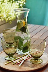 Glasses and bottle filled with water and lemon balm. Standing on a round wooden tray on wooden...