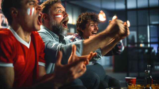 At Home Three Joyfuls Sports Fans with Painted Faces Sitting on a Couch Watch Game on TV, Celebrate Victory when Sports Team Wins Championship. Friends Cheer, Shout. Close-up Portrait Shot