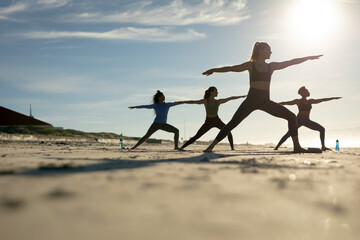 Group of diverse female friends practicing yoga at the beach