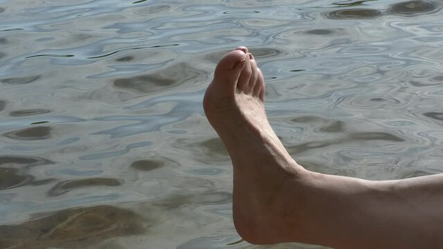 Closeup shot of a caucasian womens toes with painted nails. Water in the background. Enjoying the good weather at a lake on a sunny day. 