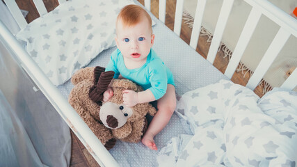 high angle view of barefoot infant boy playing in teddy bear in baby crib - obrazy, fototapety, plakaty