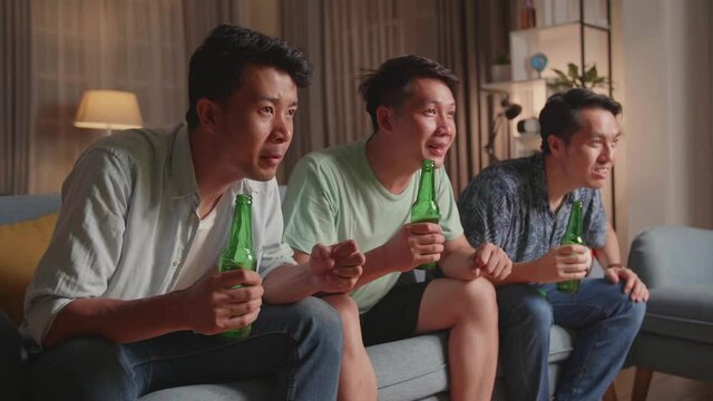 Three Asian Males Cheering And Watching Football Game On Tv And Celebrating Victory At Home
