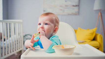 infant boy with blue eyes sitting in feeding chair and eating baby food