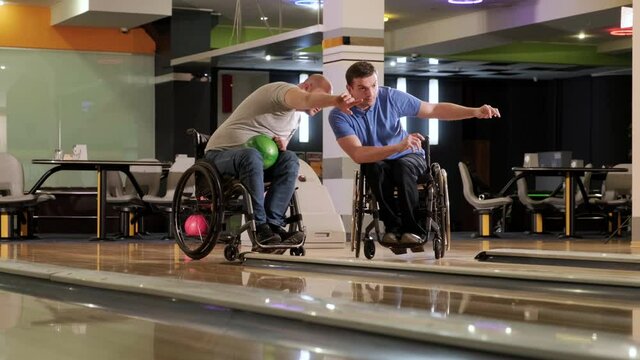 Two young disabled men in wheelchairs playing bowling in the club