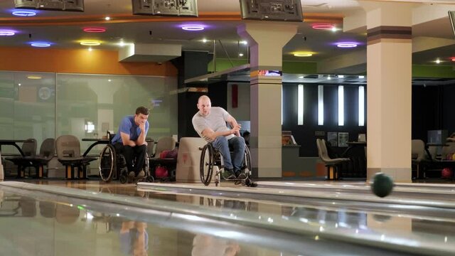 Two young disabled men in wheelchairs playing bowling in the club