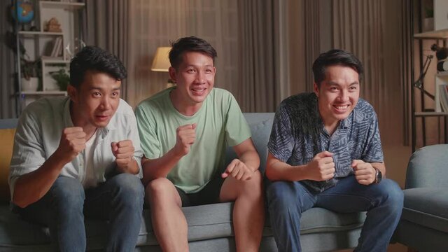 Three Asian Males Cheering And Watching Football Game On Tv And Celebrating Victory At Home
