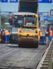 Process of asphalting and paving, asphalt paver machine and steam road roller during road construction and repairing works, workers working on the new road construction site, placing a layer in summer