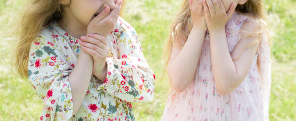 Obraz premium Two cute girls laughing, covering their mouths with the palms of their hands in the street