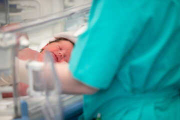 The doctor's hands in rubber gloves are holding the head of a newborn baby who lies in the medical box.