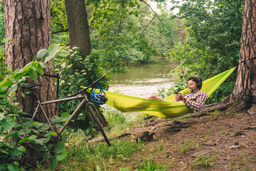 Young caucasian man resting in hammock, listening to music on headphones and using smartphone...