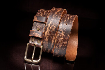 Brown leather belt with scuffs and a metal buckle on a dark background.