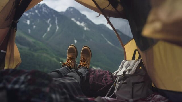 Women's legs in yellow hiking boots lie in a yellow tent. The traveler is resting, admiring the mountains after climbing. Yellow boots against the background of big mountains. Rest in the camp.