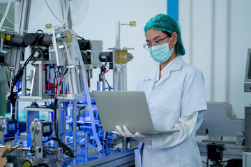 Factory worker woman with gown and hygiene mask hold laptop to control the machine in factory workplace.