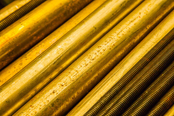 Large bronze round bars and steel threaded rods lie on a shelf, close-up.