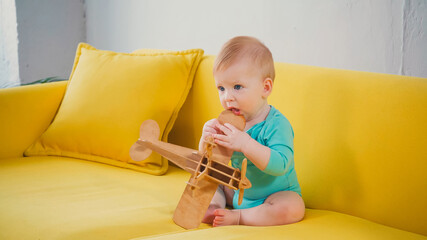 infant boy sitting on couch and playing with wooden biplane