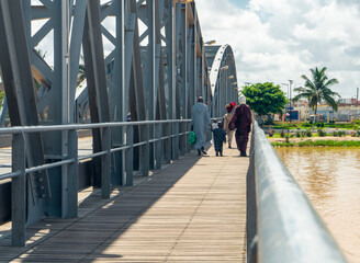 Local people walking on old the metallic arched bridge over the senegal river, called "pont faidherve" in french, located in saint Louis city, northern Senegal, West Africa.