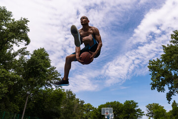 Young man, muscular african male basketball player playing basketball at street public stadium, sport court or palyground outdoors. Summer sport games.