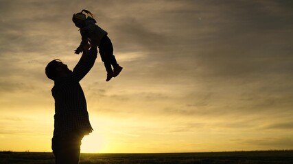 Silhouette Dad tosses his happy daughter into blue sky. Happy family holiday. Father and little child play, laugh, hug together. Enjoyable family travel. Baby is in arms of the parents. Dad's day off