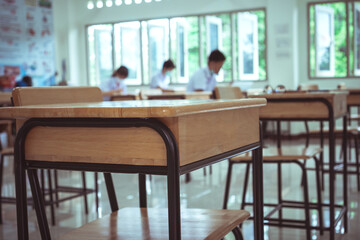 Class room tables and chairs with Paper documents of exam test on desk in examination school while blur asian girls students taking reading for testing in classroom school, Student uniform in Thailand