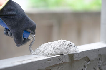 hand of industrial bricklayer hold aluminium trowel scoop mortar powder put on a brick block wall...