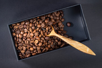 Roasted coffee beans in a black box with a wooden spoon, top view