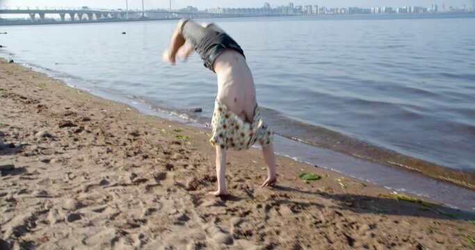 a man jumps somersaults along the shore on a beach near the sea for joy, wearing a hawaiian shirt and shorts