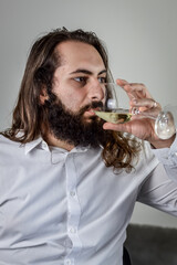 portrait of a young middle eastern businessman with beard and long hair drinking a glass of fresh white wine