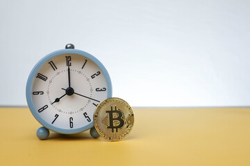 A Bitcoin standing against an alarm clock isolated on the  yellow background 