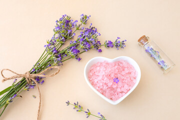 Obraz na płótnie Canvas pink sea salt in a heart-shaped plate, small bottle and lavender on beige background. Spa concept