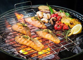 Grilled salmon fish with various vegetables on pan on the flaming grill pepper lemon and salt, herb decoration. Selective focus. Healthy meal concept.