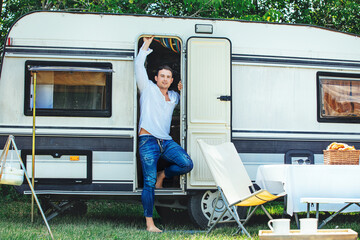 Man a young adult in jeans and a white shirt is traveling in a mobile home trailer